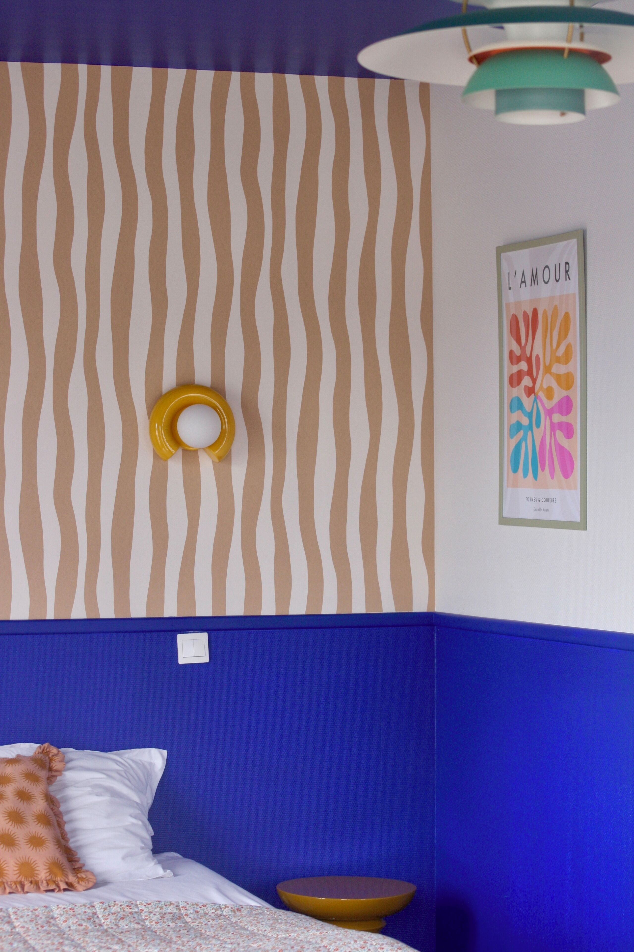 A bedroom with a striped wall pattern, a framed artwork titled "L'AMOUR," and a bed with a white and orange pillow.