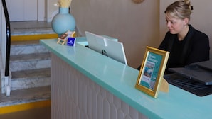 Un taulell de recepció amb un ordinador, un plafó informatiu de les habitacions i miralls decoratius a la paret.