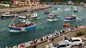Zona de front marítim amb vaixells, una multitud i un edifici amb teulada vermella.