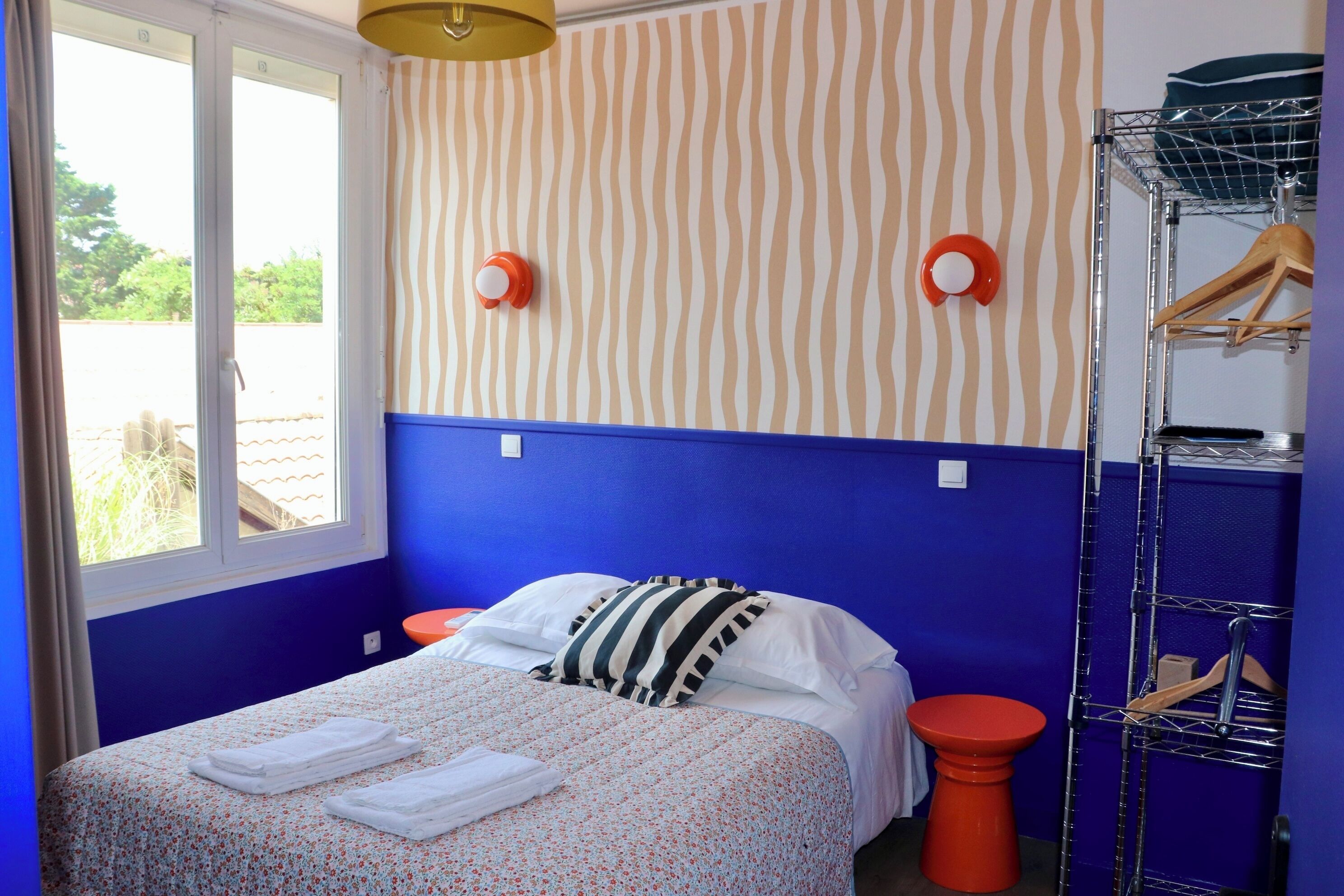 Un dormitorio con cama, ventana, pared con diseño a rayas y un perchero metálico.