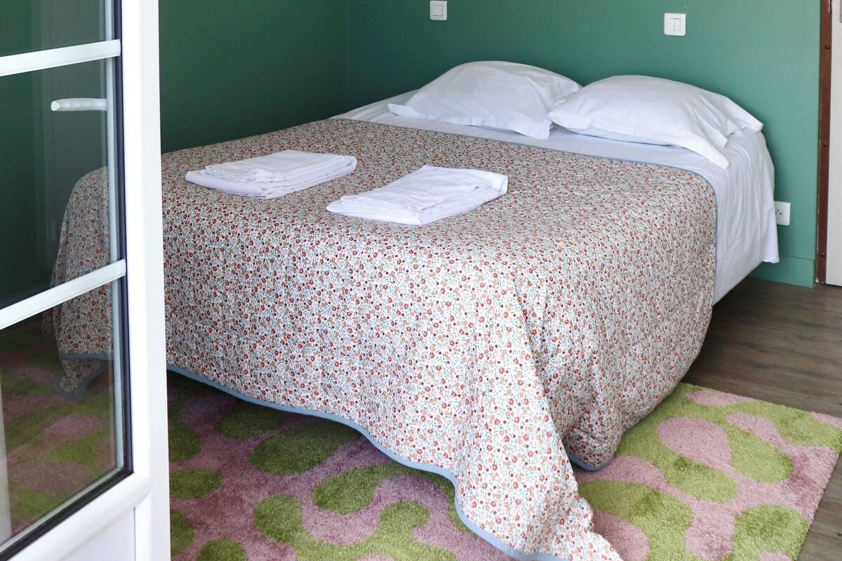 A bedroom with a bed, a woven ceiling light, a wall-mounted air conditioner, and a framed picture.