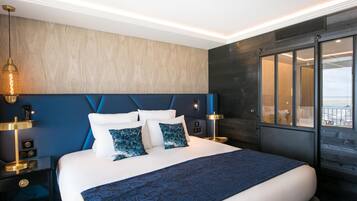 Habitación de hotel moderna con una cama grande, vista al océano y un paisaje urbano visible a través de la ventana.