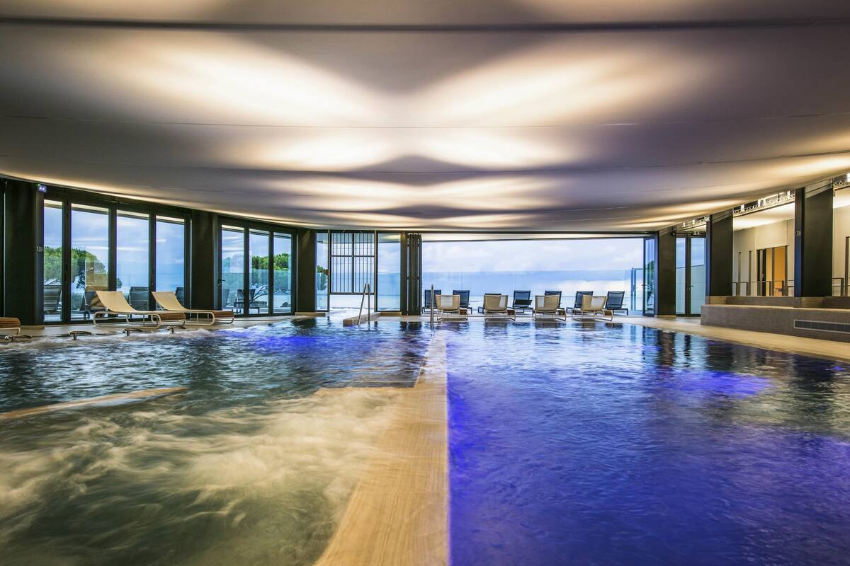 An indoor swimming pool with lounge chairs and a view of the ocean.