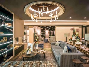 A modern living room with a central seating area, a bookshelf, and a decorative chandelier. - La Grande Terrasse Hotel & Spa La Rochelle - MGallery Collection (Chatelaillon-Plage)