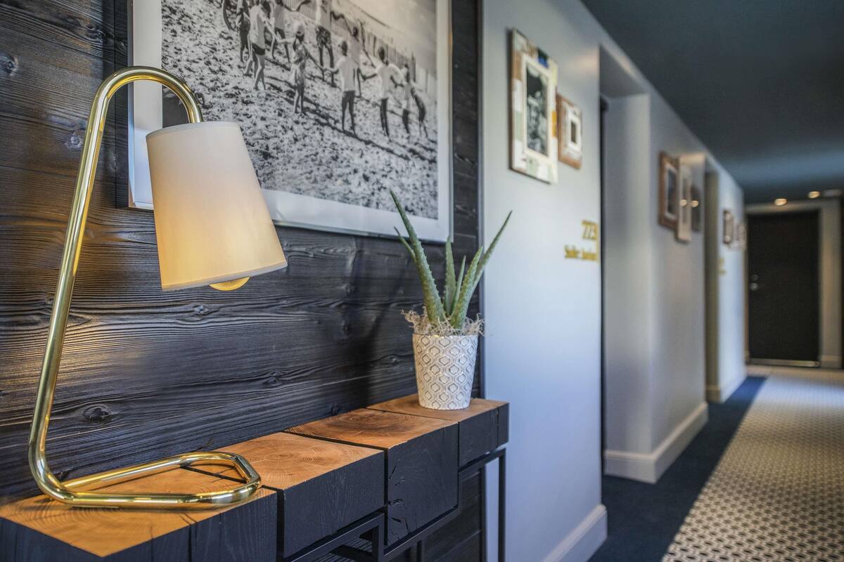 A hallway with a wooden console table, a floor lamp, a potted plant, and framed pictures on the wall.