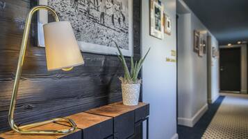 A hallway with a wooden console table, a floor lamp, a potted plant, and framed pictures on the wall.
