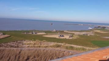 Ein Küsten-Golfplatz mit Bunkern, einem Holzzaun und Blick auf das Meer.