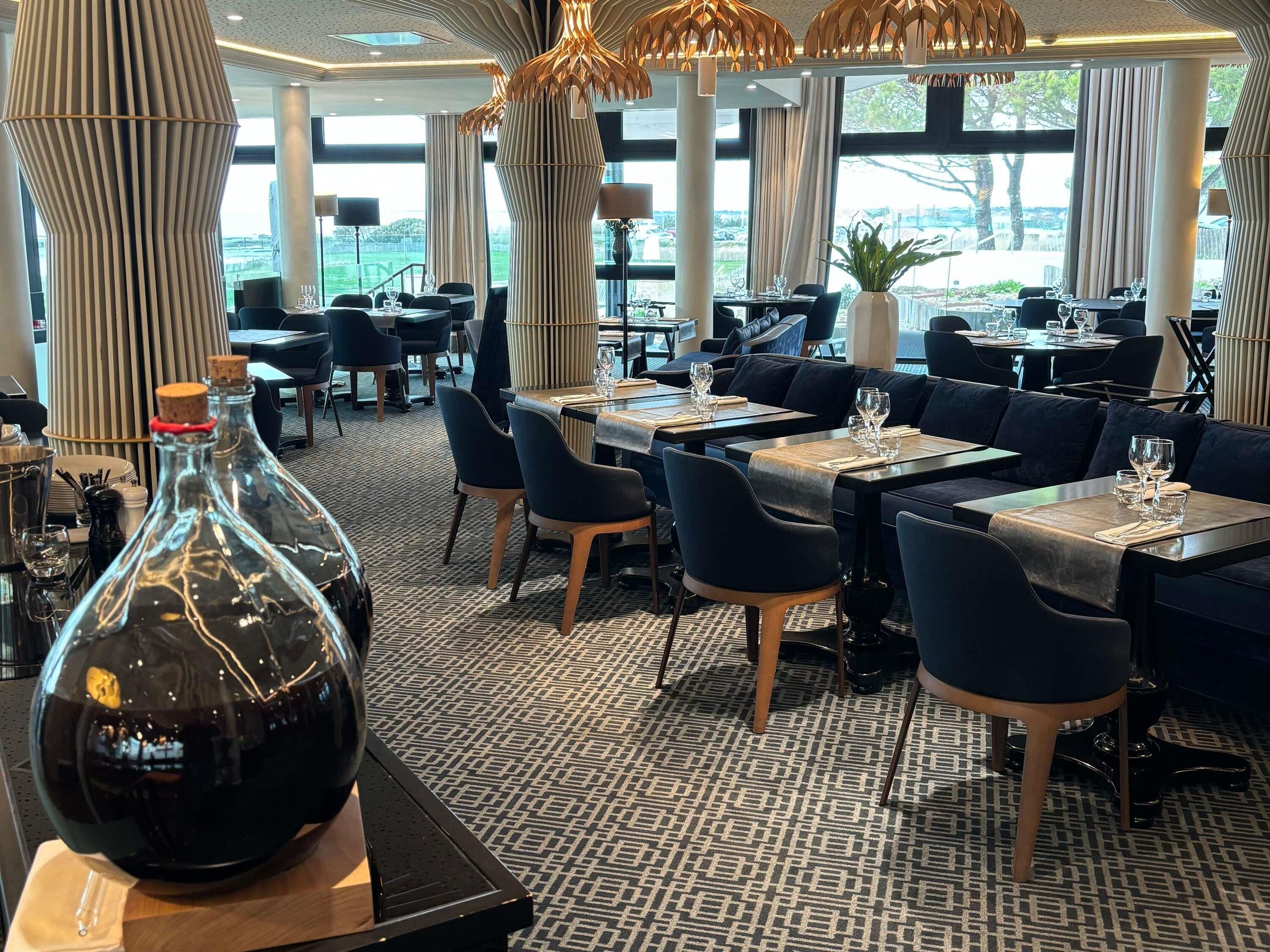 A modern restaurant with a patterned carpet, black and wooden furniture, and large windows offering a view of the outdoors.