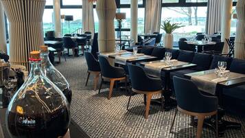 A modern restaurant with a patterned carpet, black and wooden furniture, and large windows offering a view of the outdoors.