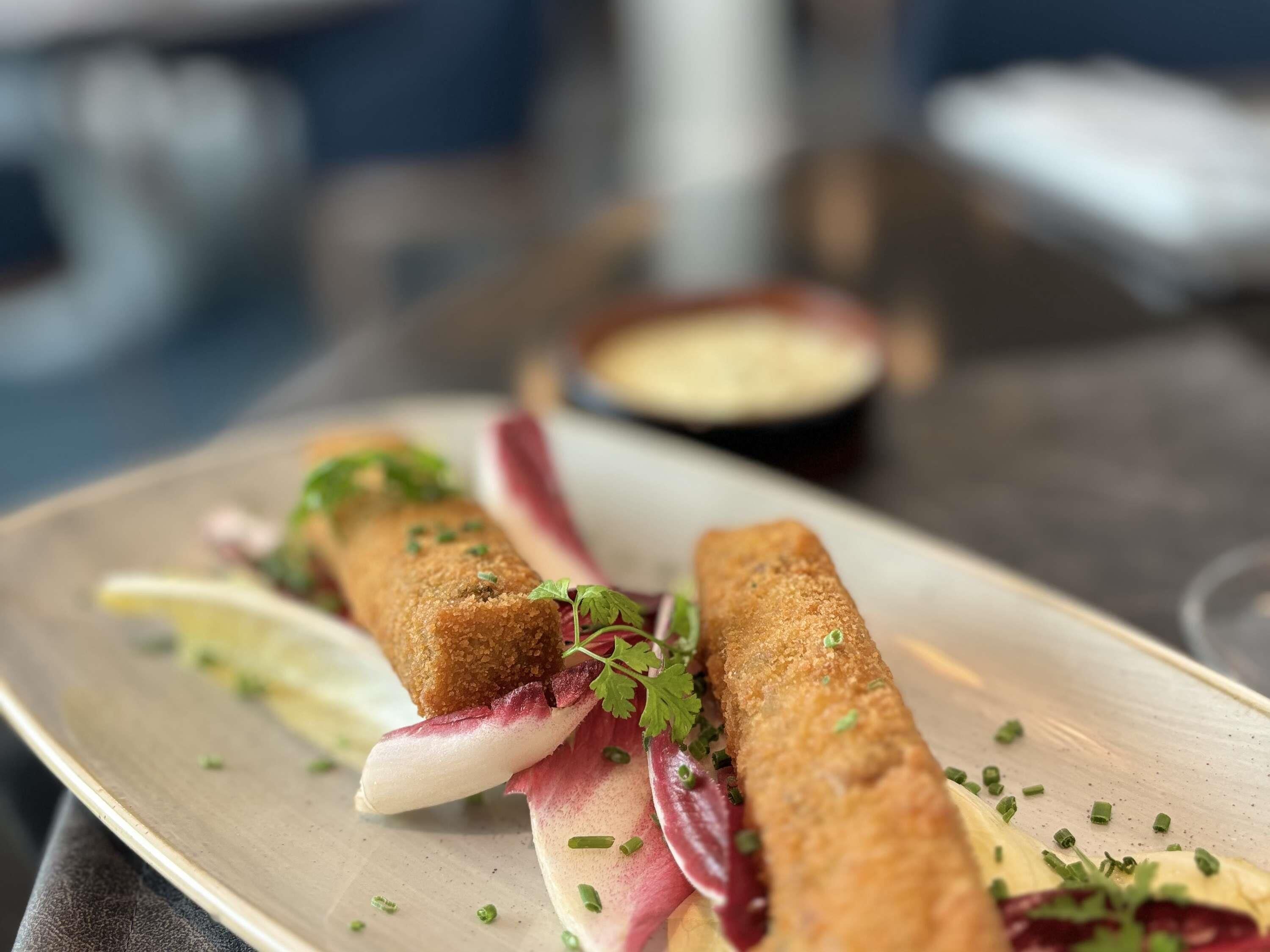 A plate with two breaded rolls, garnished with herbs, accompanied by radish slices and a lemon wedge.
