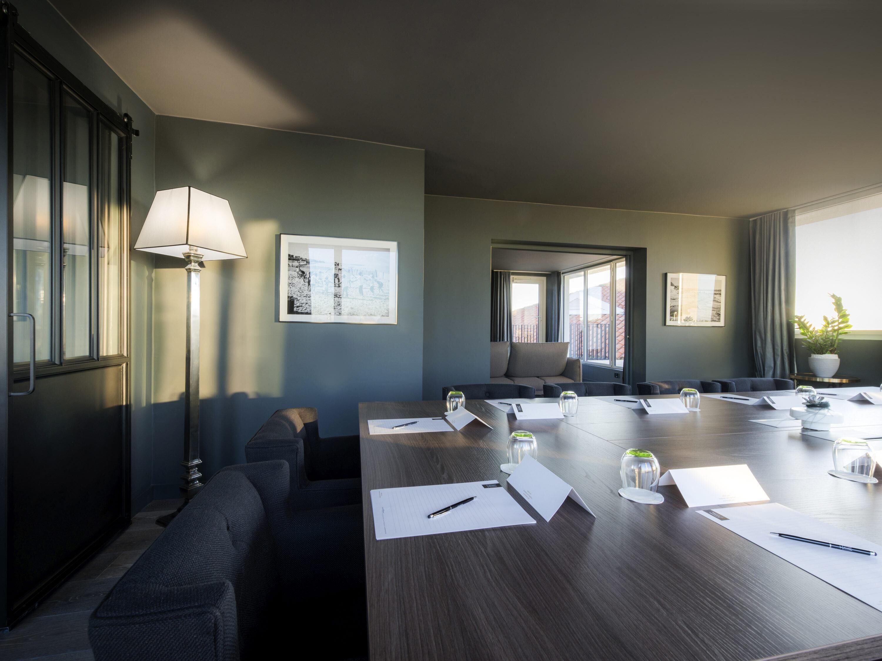 A conference room with a long table, chairs, a lamp, and framed pictures on the walls.
