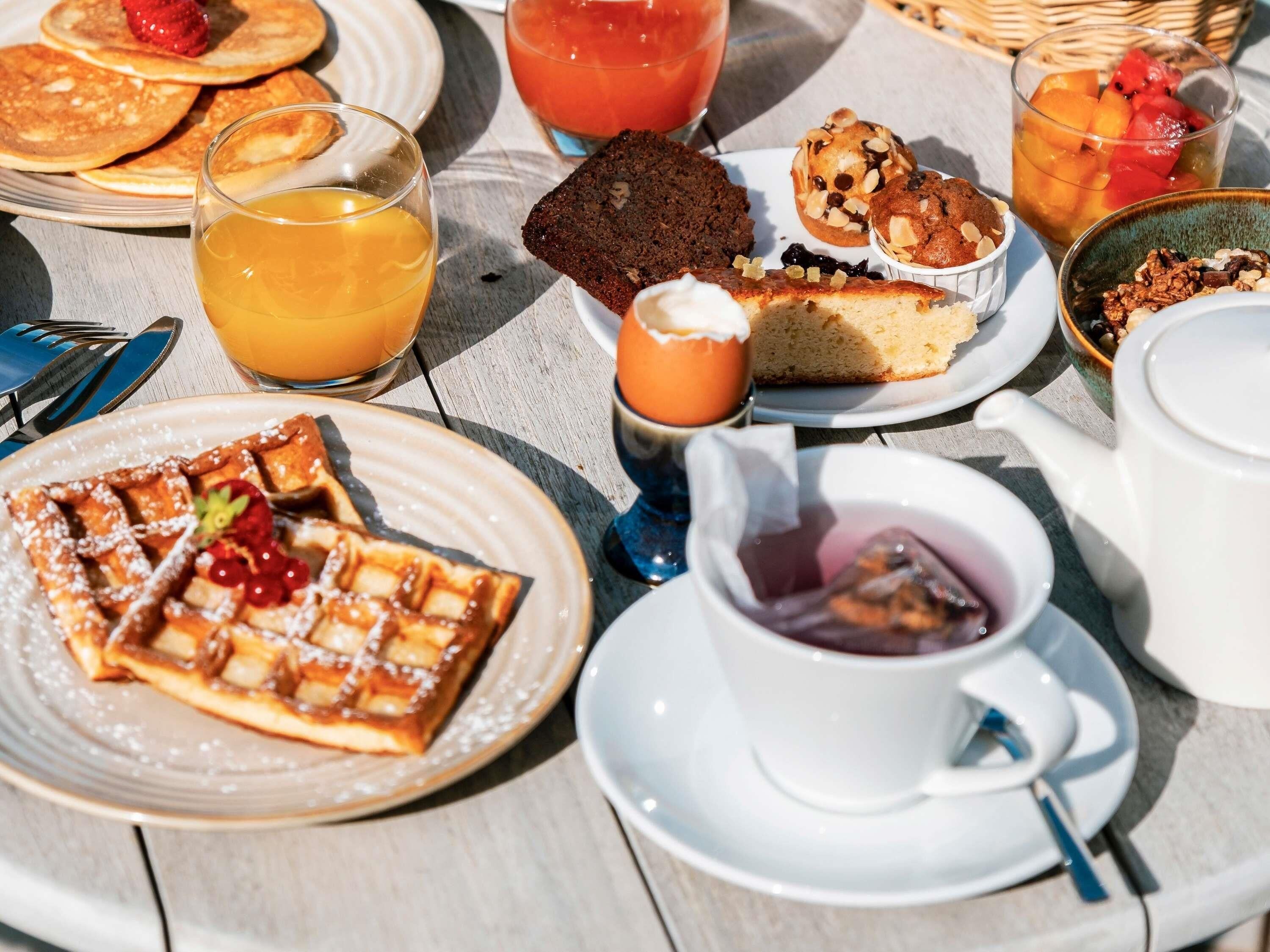 A breakfast table with waffles, pancakes, muffins, and a variety of beverages.