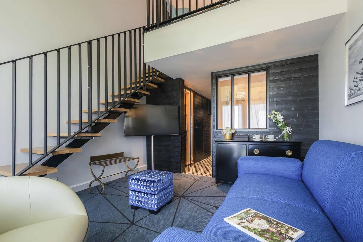 A modern living room with a staircase, a sofa, a bench, and a small table with a vase.
