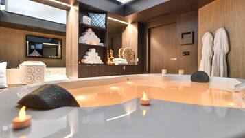 A modern spa room with a hot tub, towels, and a shelf with toiletries.