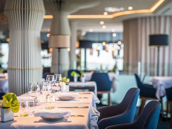 A dining area with tables set for a meal, chairs, and a large pillar. - La Grande Terrasse Hotel & Spa La Rochelle - MGallery Collection (Chatelaillon-Plage)