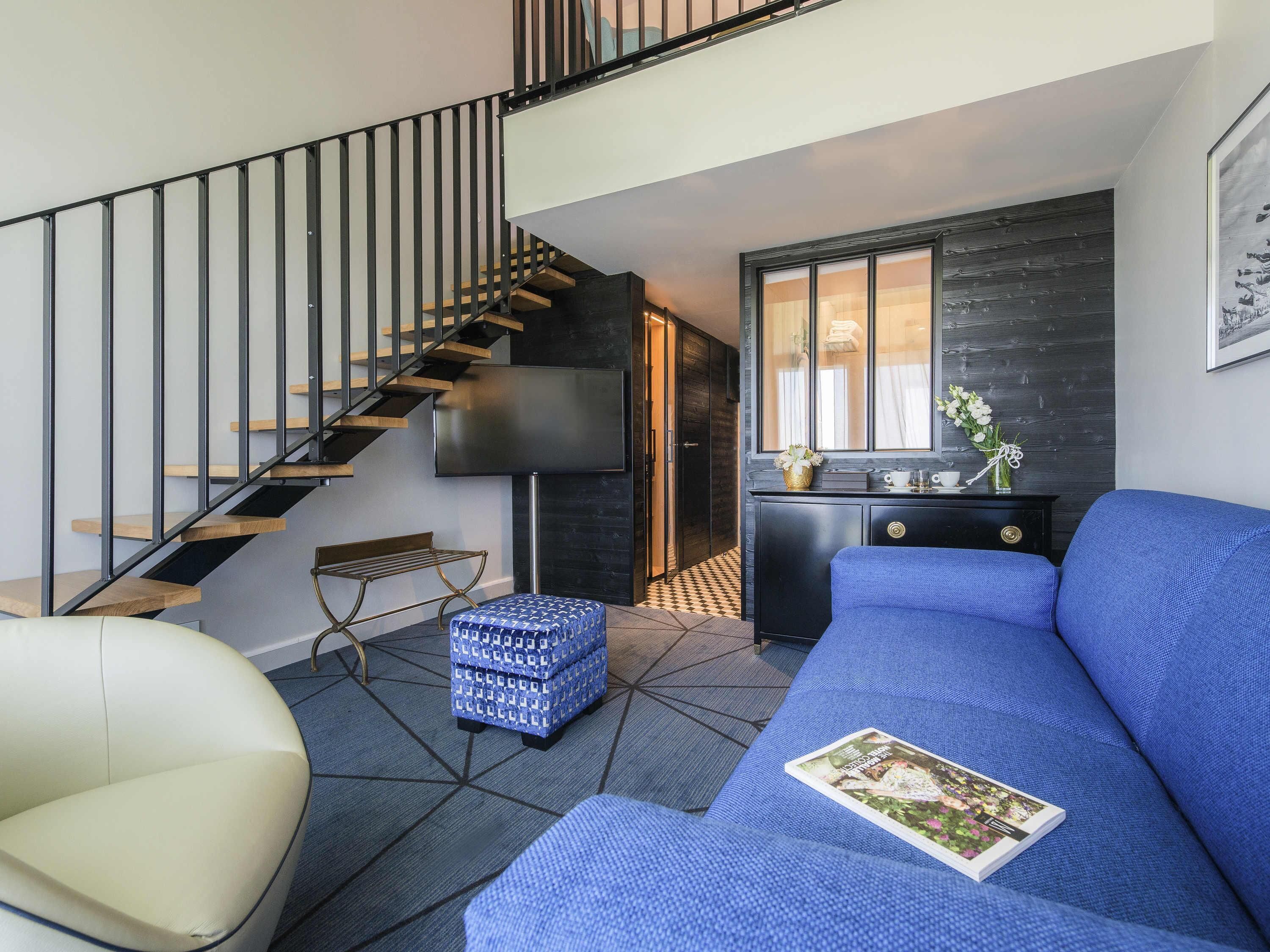 A modern living room with a staircase, a sofa, a bench, and a small table with a vase.