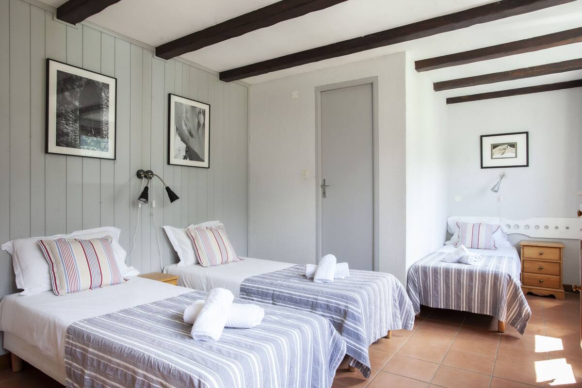 Habitación de hotel con tres camas, techo de madera y dos cuadros enmarcados en la pared.