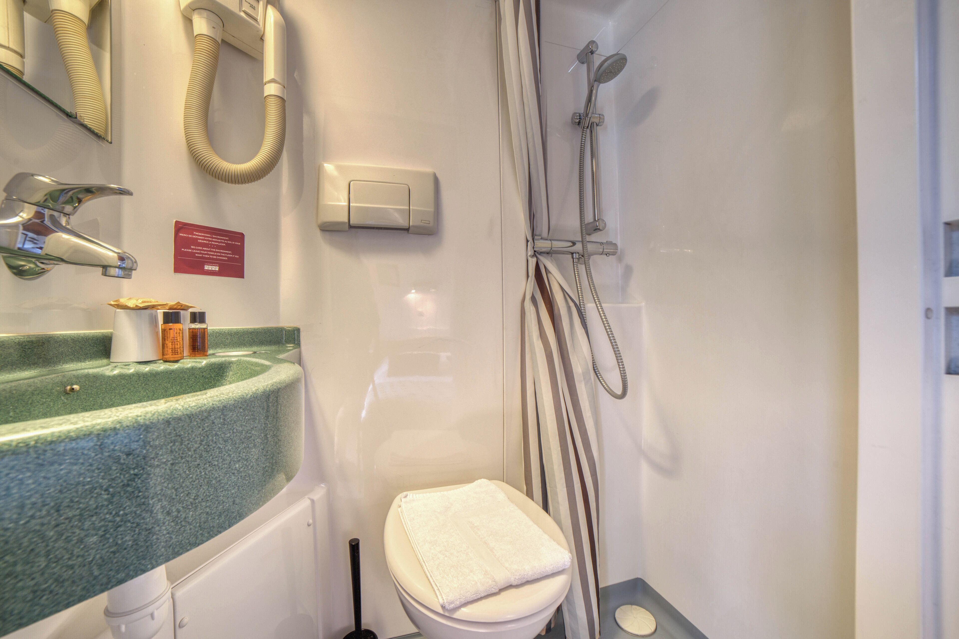 A bathroom with a green sink, a toilet, a shower with a handheld showerhead, and a towel rack.