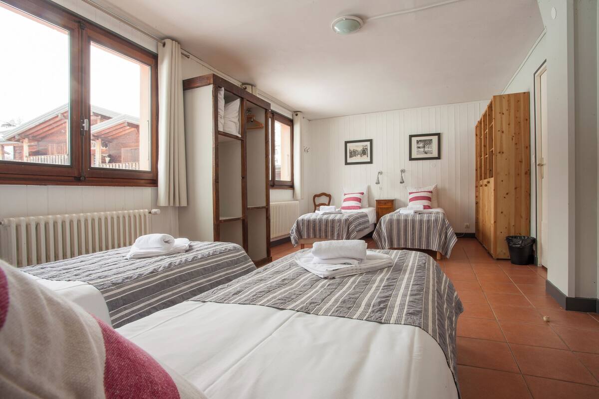 Una habitación de hotel con dos camas, un armario de madera, un radiador y una ventana con cortinas.
