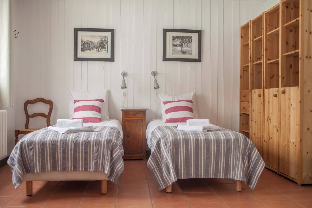 Una habitación con dos camas, un armario de madera y dos cuadros enmarcados en la pared.