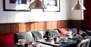 A dining area with wooden paneling, a bench with red and grey cushions, and a table set with plates, bowls, and glasses.
