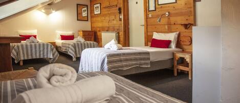 Una habitación acogedora con tres camas, paredes de madera y techo inclinado.