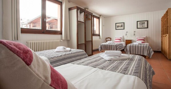 A hotel room with two beds, a wooden wardrobe, and a window with curtains.