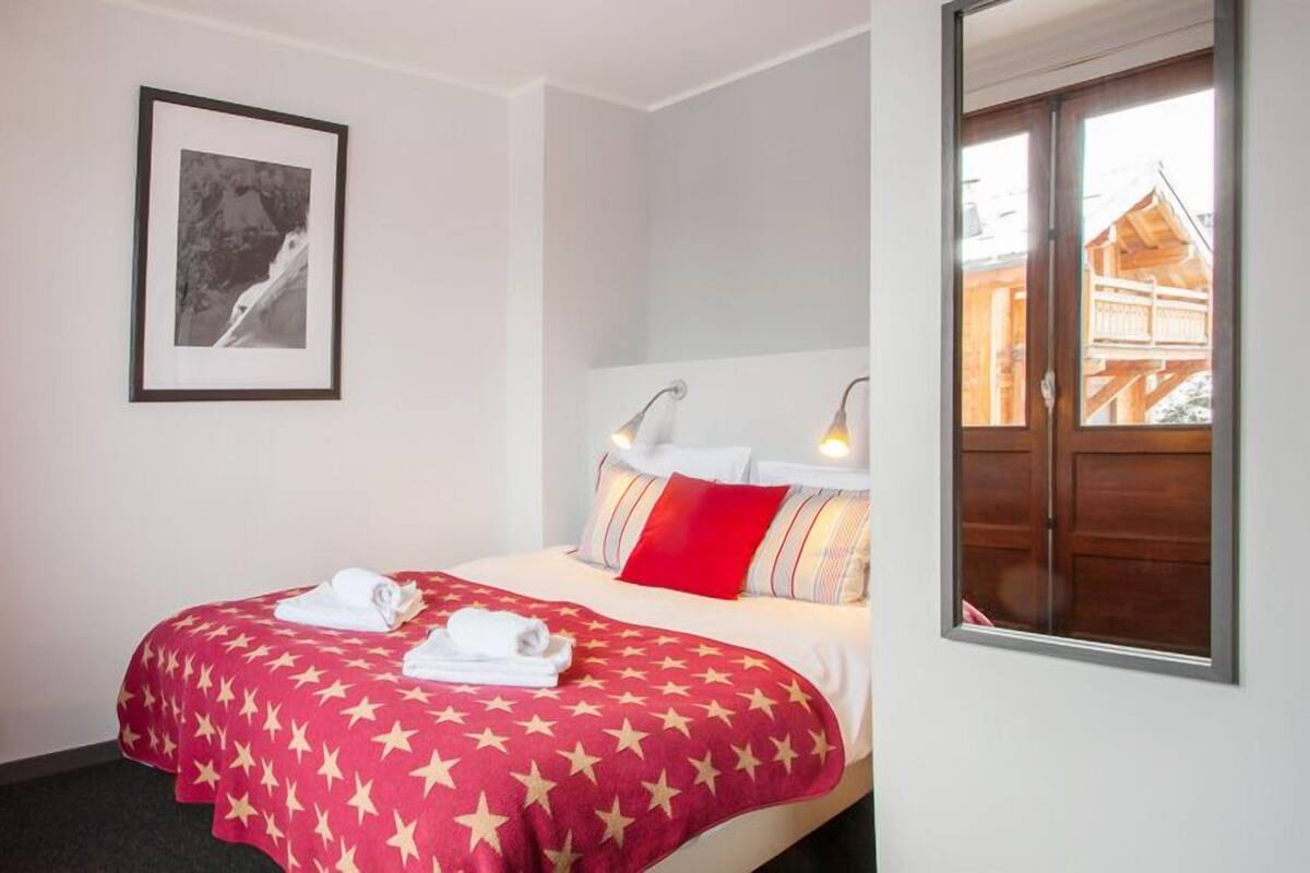 Habitación de hotel con cama, una silla, un cuadro en la pared y ventana con vista a un edificio.