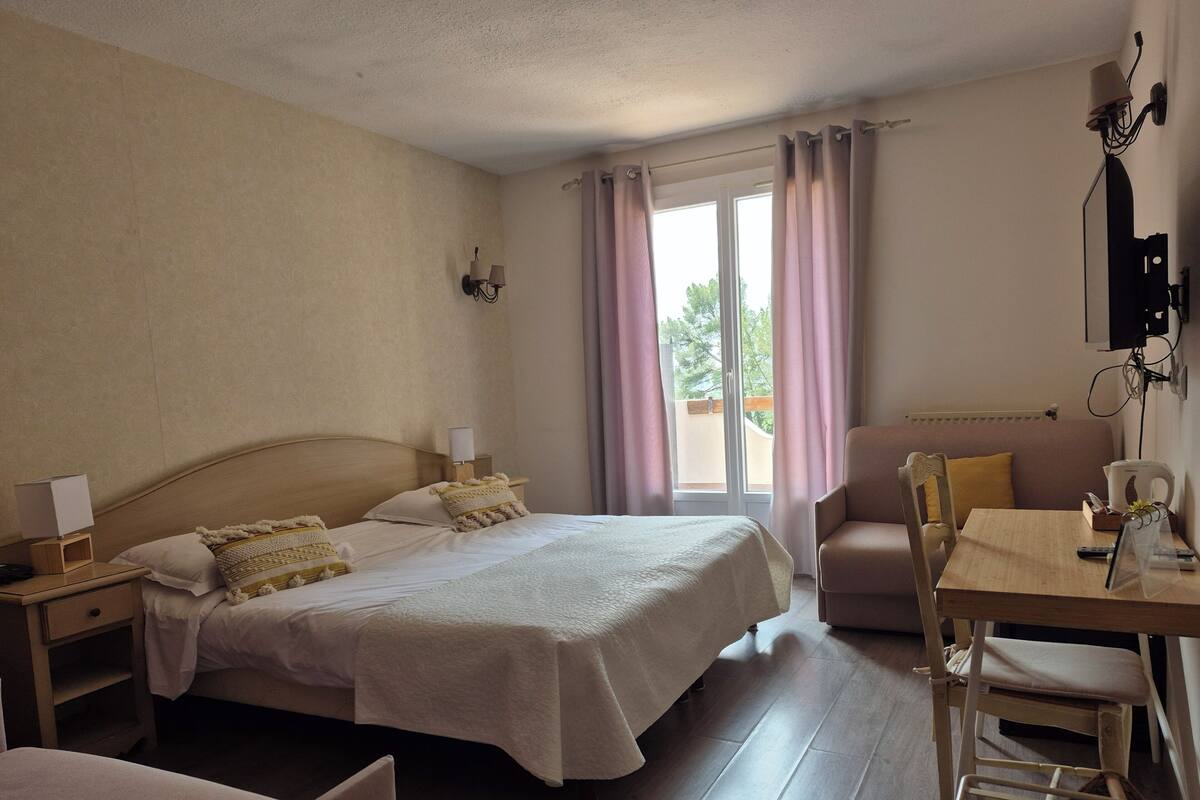 Ein Hotelzimmer mit Bett, Nachttischen, einem Schreibtisch mit Stuhl, einem Fernseher und einem Fenster mit Vorhängen.