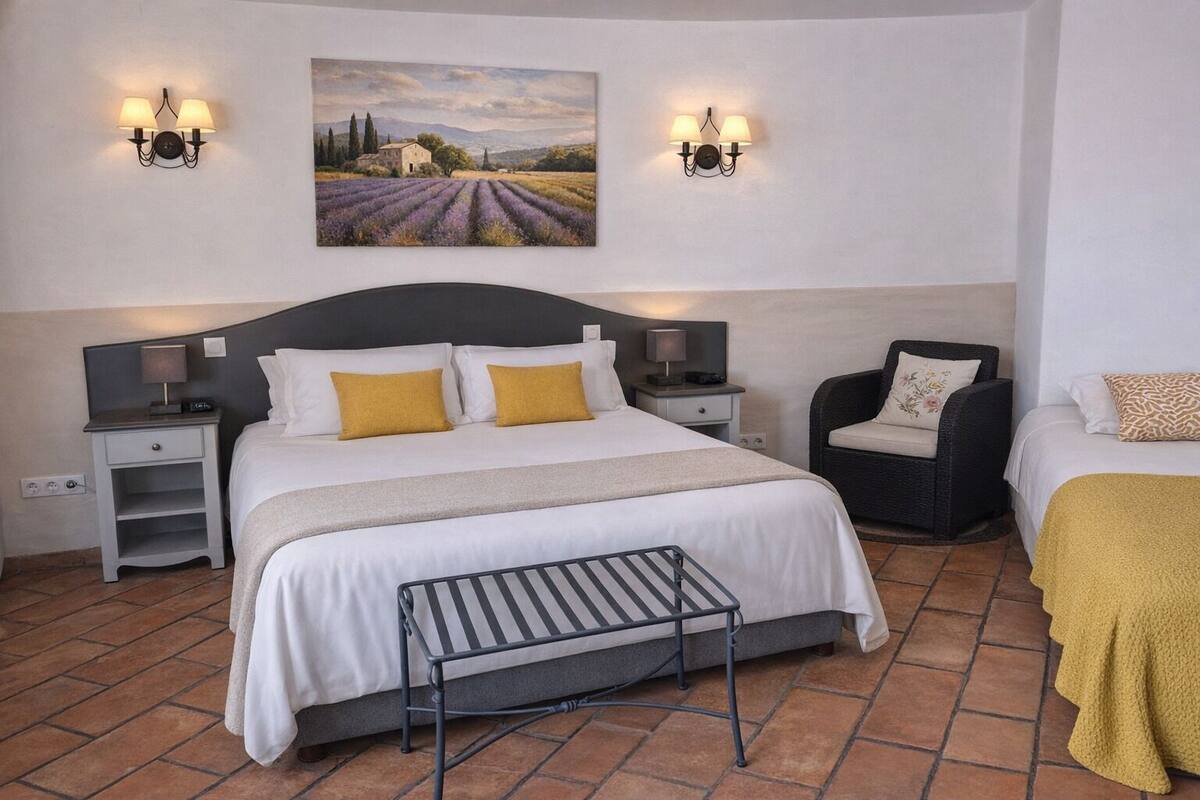 Ein Schlafzimmer mit einem großen Bett, zwei Nachttischen, einem Sessel, einem kleinen Tisch und einem Bild an der Wand.