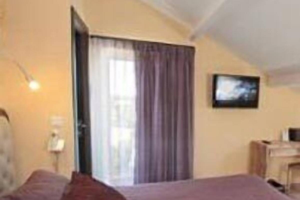 A hotel room with a large bed, a desk, a chair, a television, and a window with curtains.