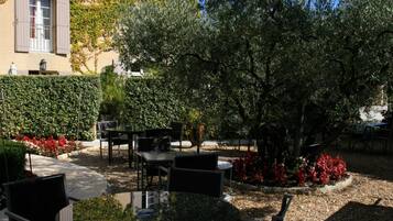 Un espacio al aire libre con mesas y sillas, rodeado de follaje y un edificio con una ventana.