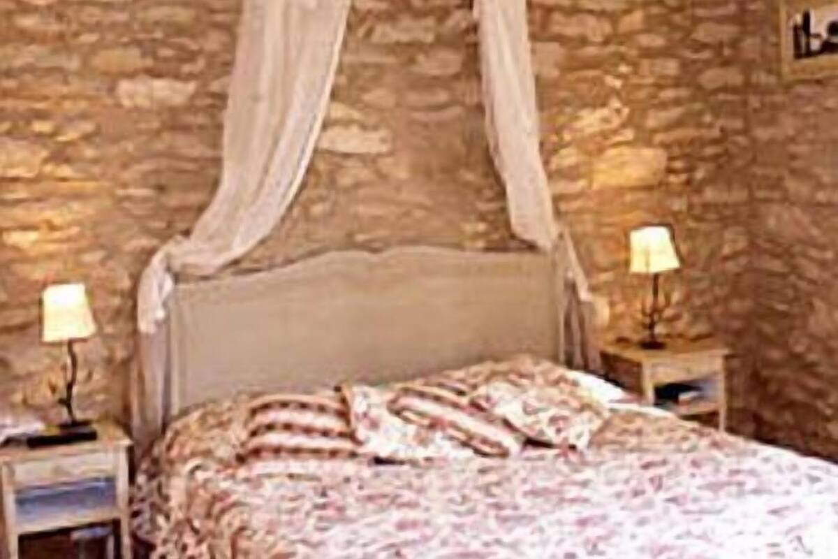 A bedroom with a stone wall, a canopy bed, two bedside tables with lamps, and a patterned bedspread.