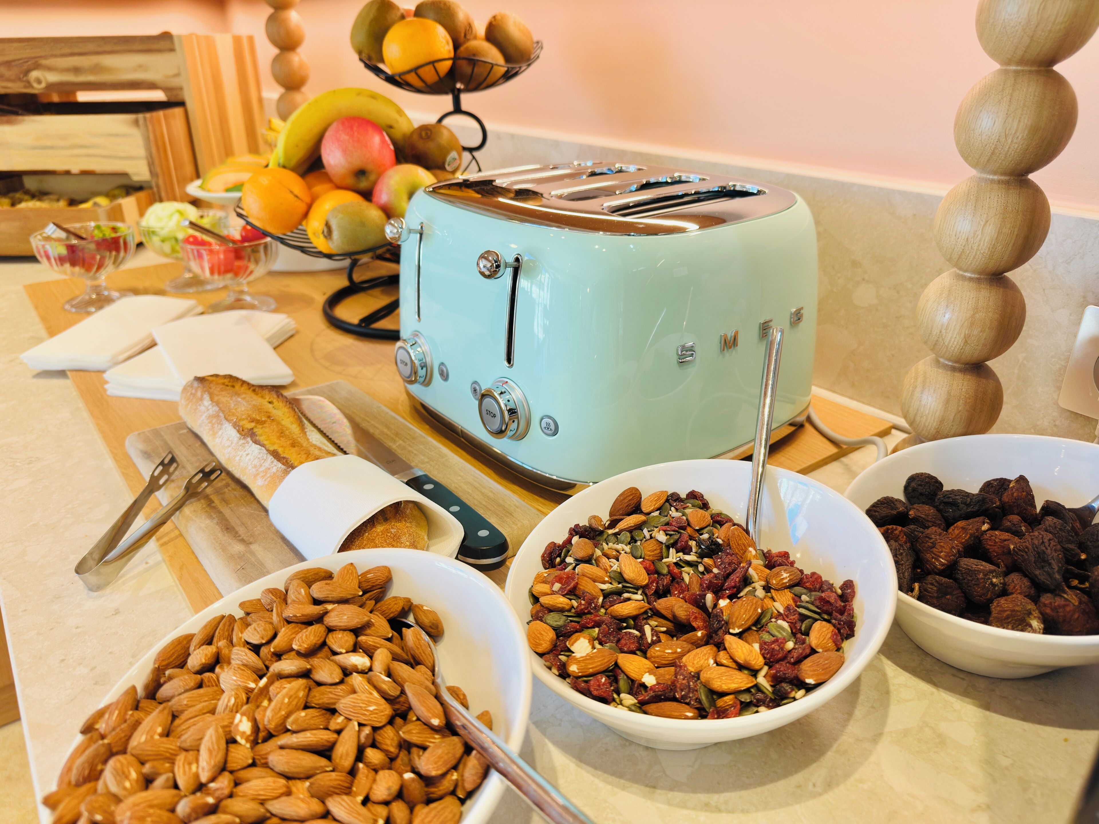 A kitchen with a vintage toaster, bowls of almonds and dried fruits, and a fruit basket.