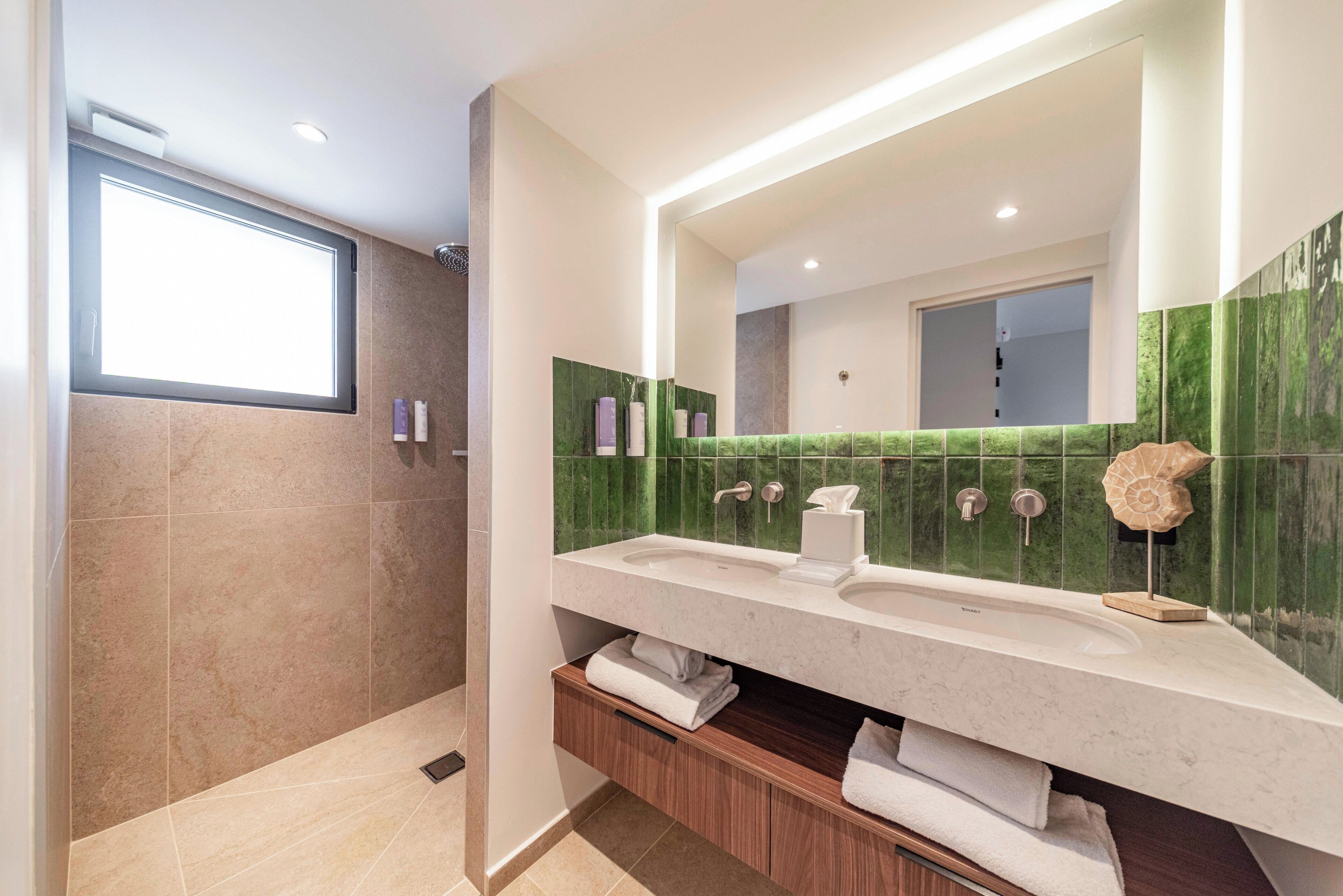 A modern bathroom with a large mirror, two sinks, and a shower area.