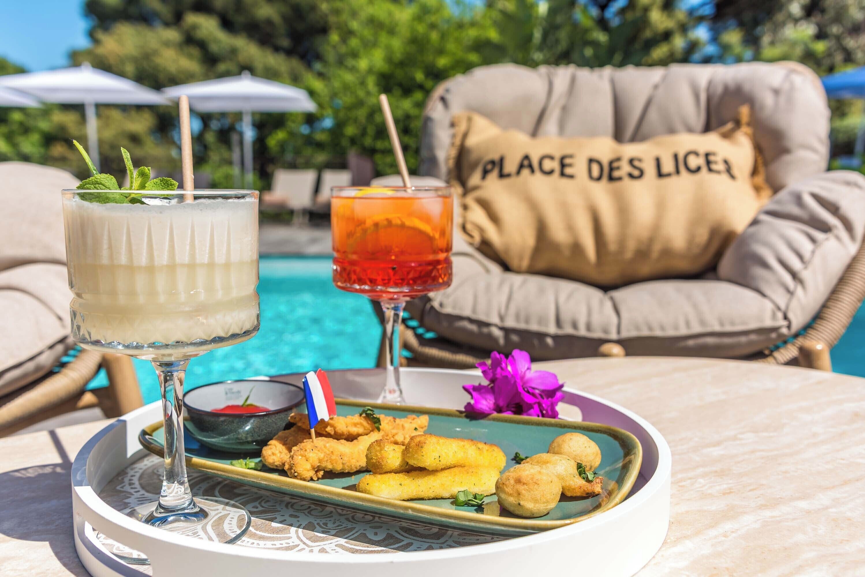 A table with a drink, a plate of food, and a cushion with 'PLACE DES LICES' text.