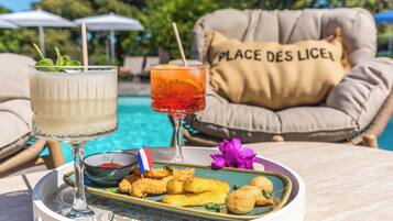 A table with a drink, a plate of food, and a cushion with 'PLACE DES LICES' text.