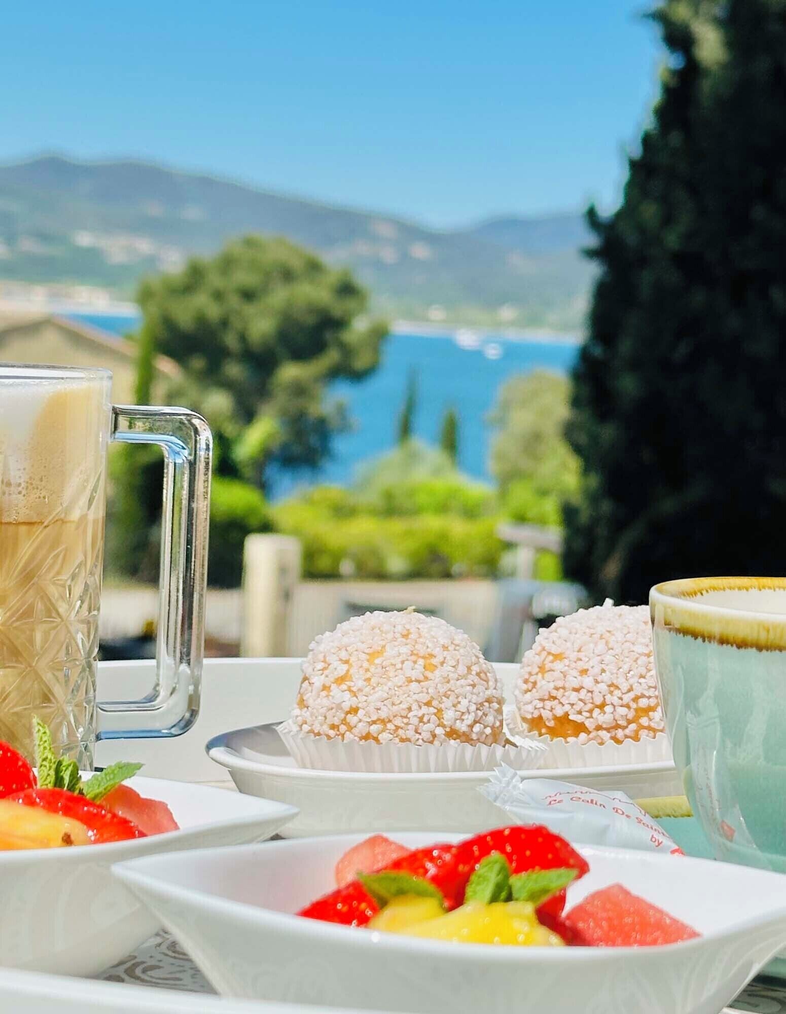 A table with food and drinks, a clear view of the sea, and a mountainous landscape.