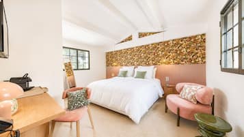 Une chambre à coucher avec un lit, un bureau, une chaise, une table de chevet et un tabouret vert.