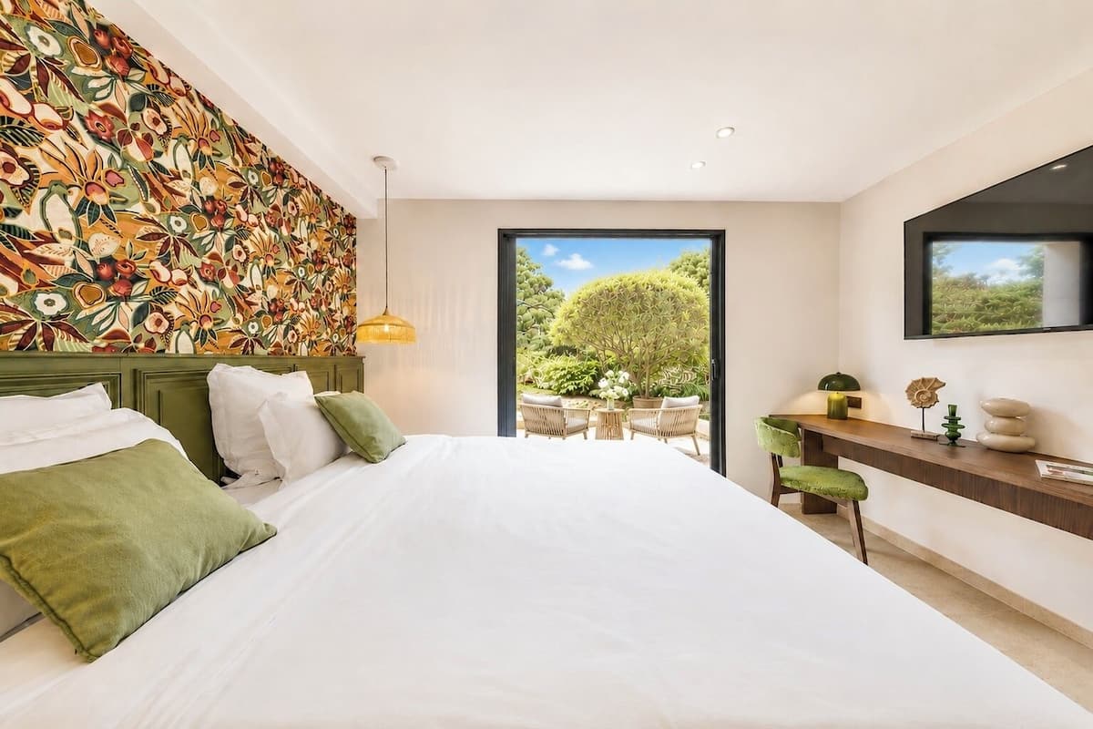 A bedroom with a large bed, a desk, and a view of the outdoors.