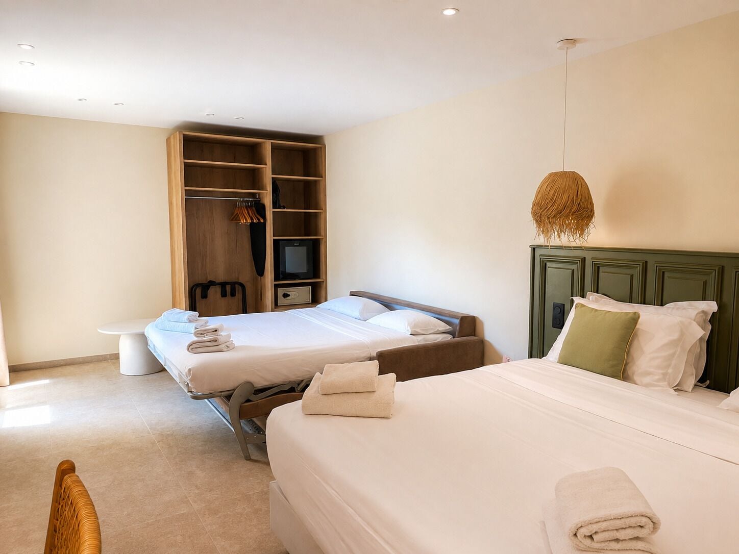 A hotel room with two beds, a television, a wardrobe, and a bench.