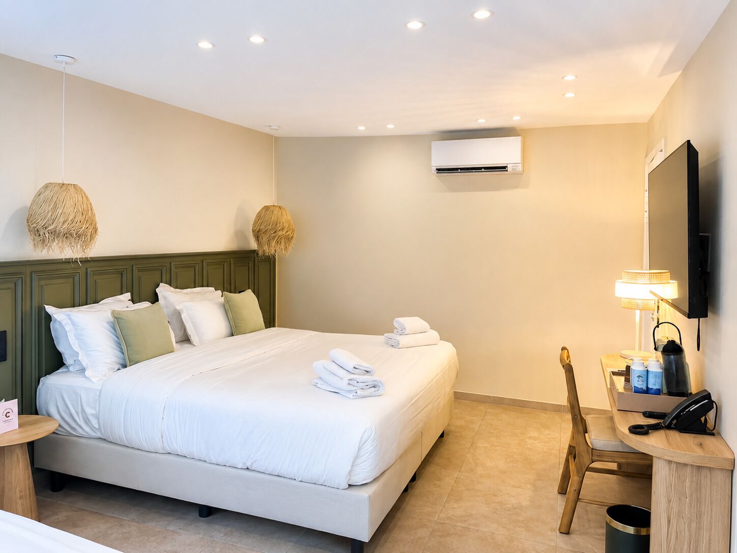 A hotel room with a bed, bedside table, lamp, and a desk with a telephone.