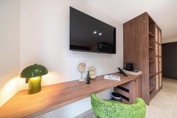 Una habitación moderna con televisión de pantalla plana montada en la pared, un escritorio de madera con lámpara, una silla verde y estanterías empotradas.