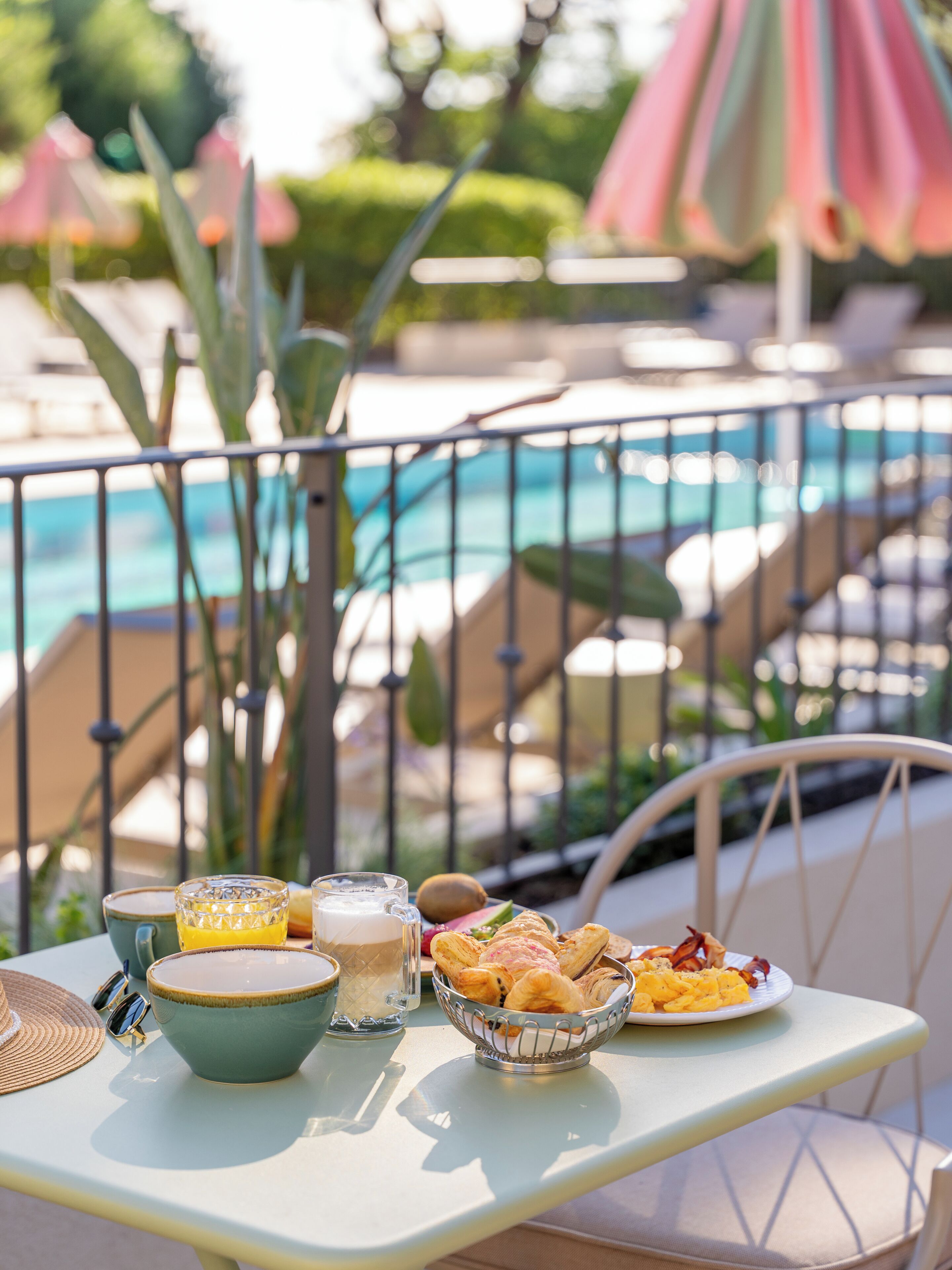 A table with food and drinks, a pool in the background, and outdoor umbrellas.