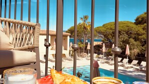 Una mesa de comedor con comida y bebidas, una piscina y vistas a un edificio y árboles.