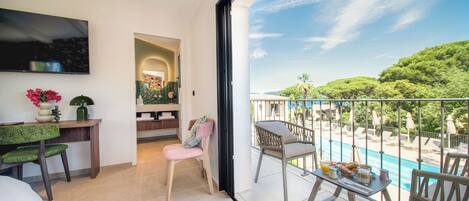 Un balcón con vista a la piscina, un televisor en la pared y un área de estar con una mesa.