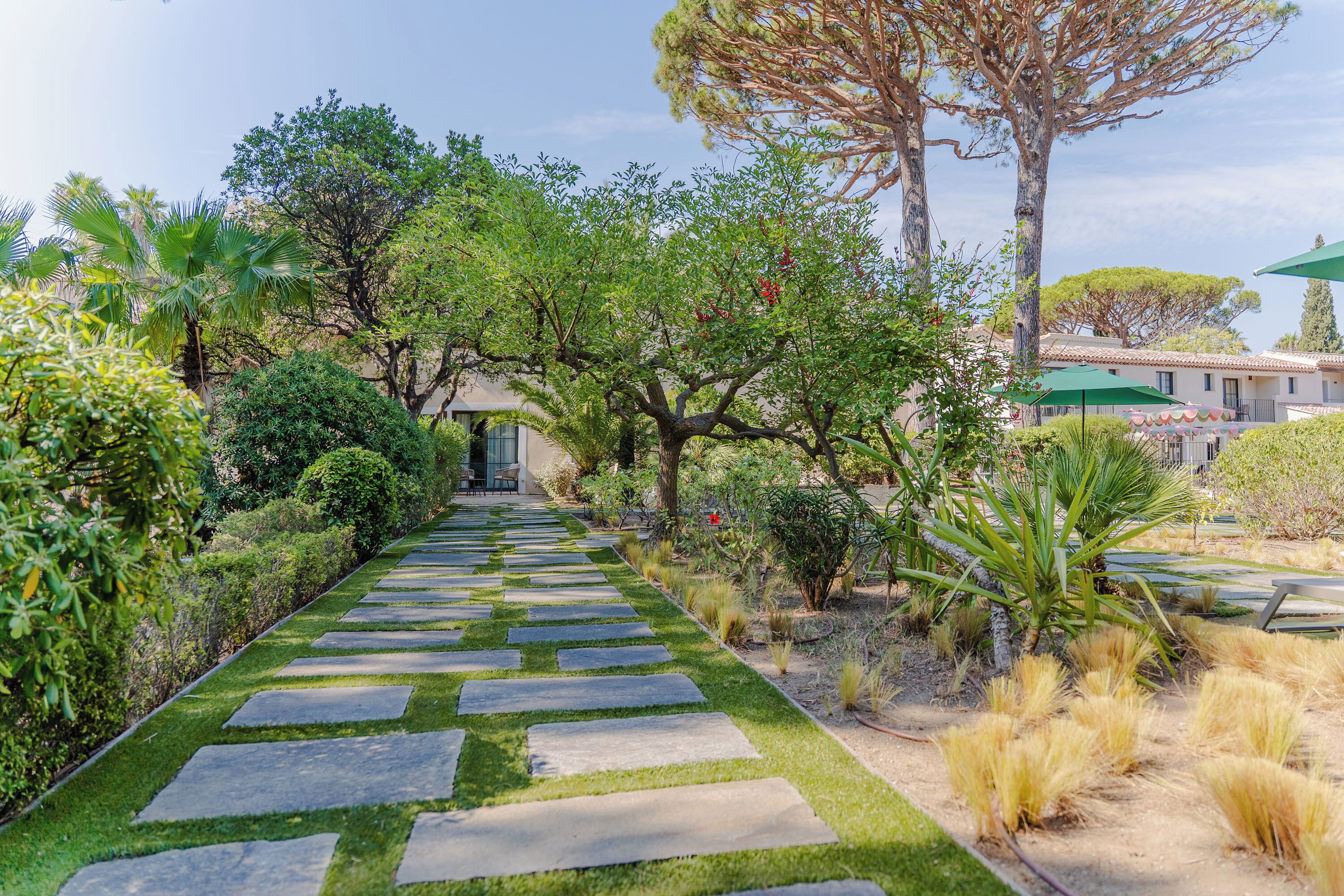 Un sendero conduce a un edificio de estilo arquitectónico tradicional, rodeado de abundante vegetación y diversas plantas.