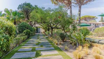 Un sendero conduce a un edificio de estilo arquitectónico tradicional, rodeado de abundante vegetación y diversas plantas.