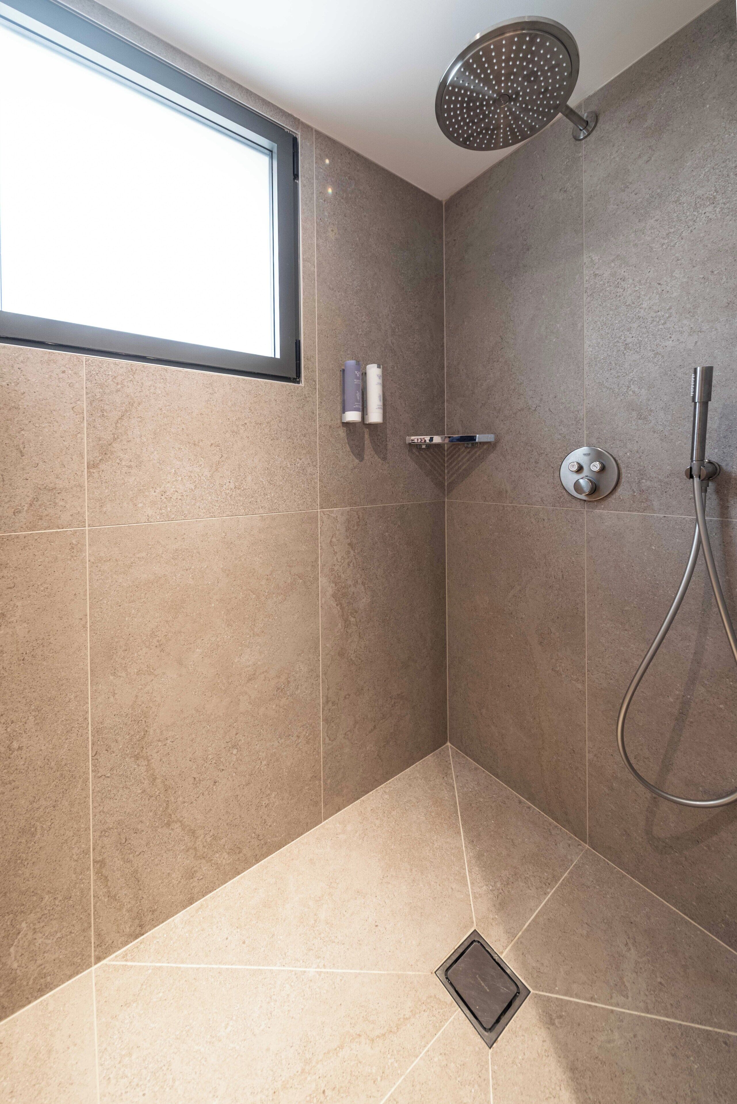 A shower with a rain shower head, a handheld showerhead, and a wall-mounted control panel.