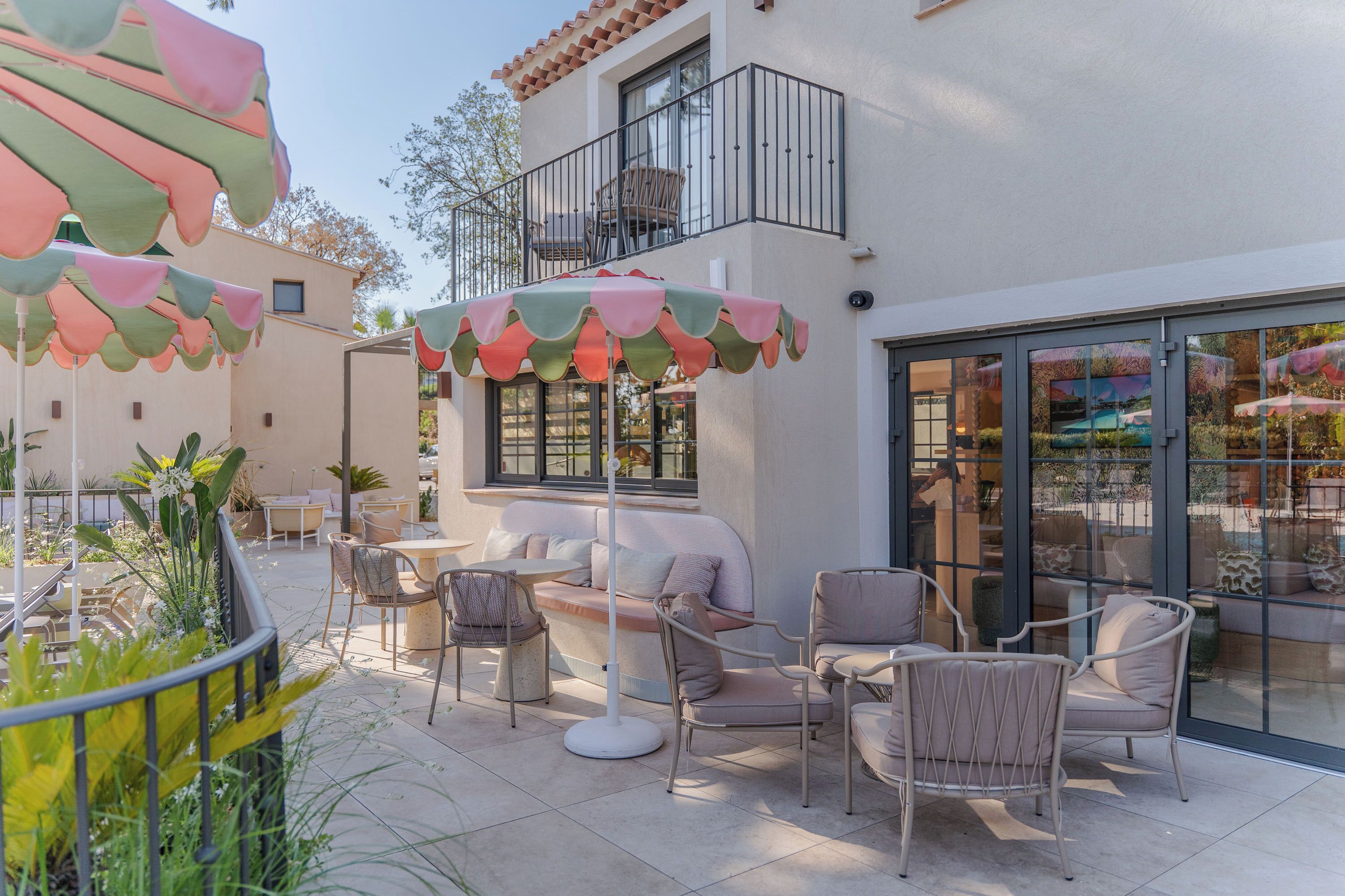 An outdoor seating area with chairs and tables, a balcony with a railing, and a building with large windows.